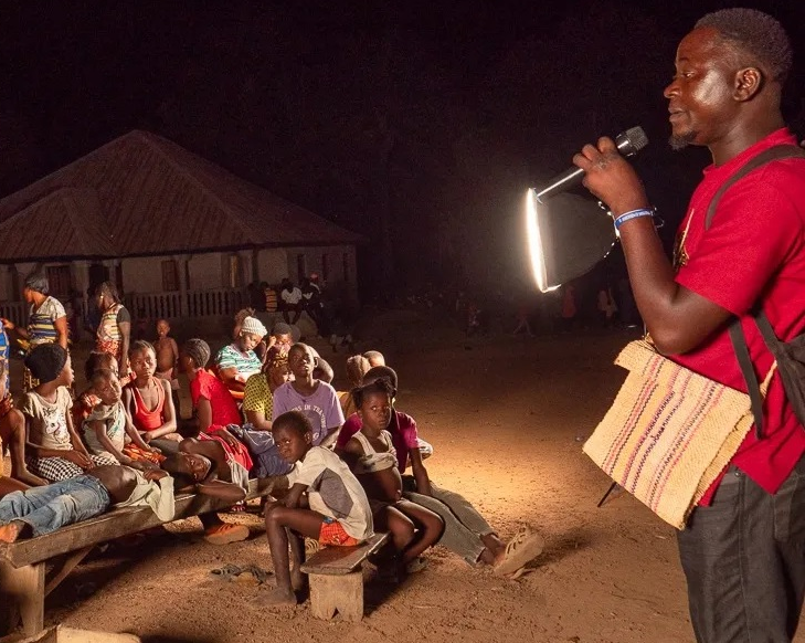 Speaking at a group of people at a film screening in Sierra Leone