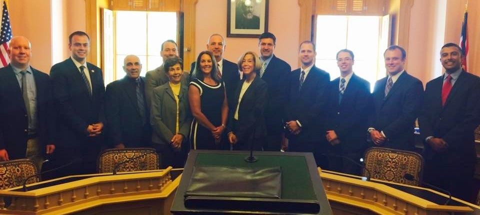 a group of people posed around a fancy table for a bill signing smiling at the camera