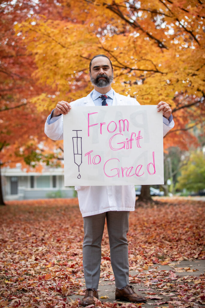 Nephrologist, Dr. Arjun Since, holds a sign reading "From Gift to Greed" before participating in a demonstration with T1I outside the Eli Lilly headquarters in Indianapolis, IN, aimed at pressuring the drug company to lower the cost of insulin, on Monday, October 24, 2022. © Photo by Erin Lubin