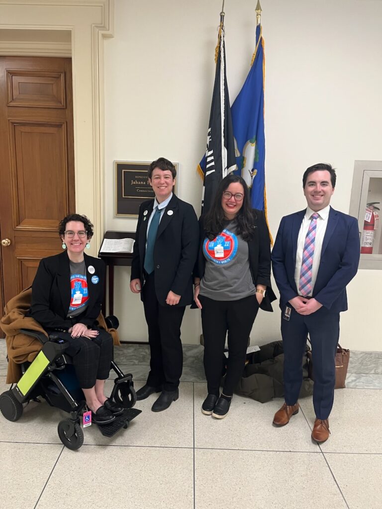 Group of people gathered near flags in hallway at US Capitol outside Representative’s office