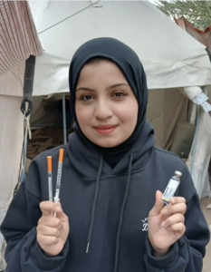 Lojain, a woman in a hijab, smiles at the camera with her insulin and syringes