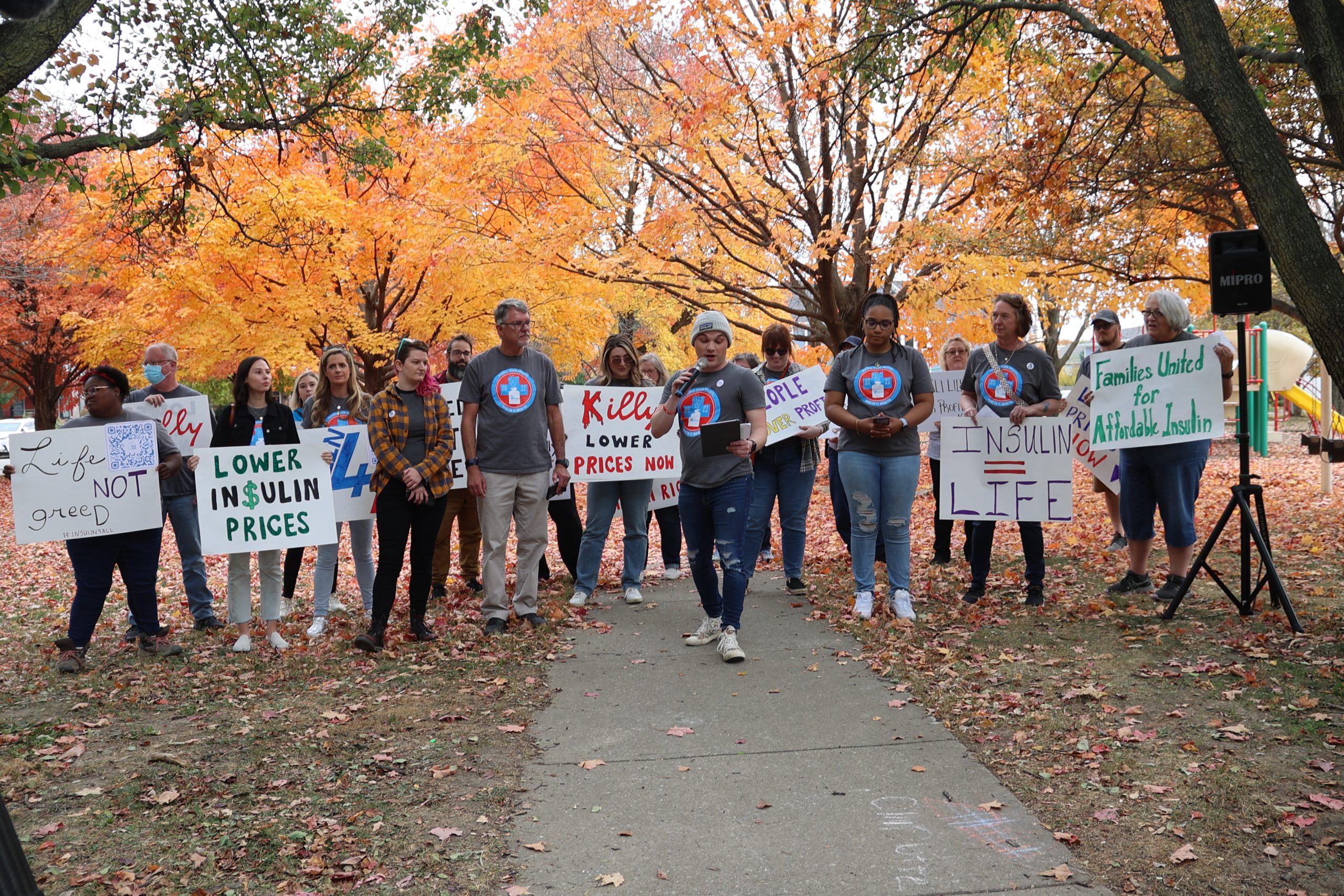 Group of advocates speaking and holding protest signs at an outdoor direct action event