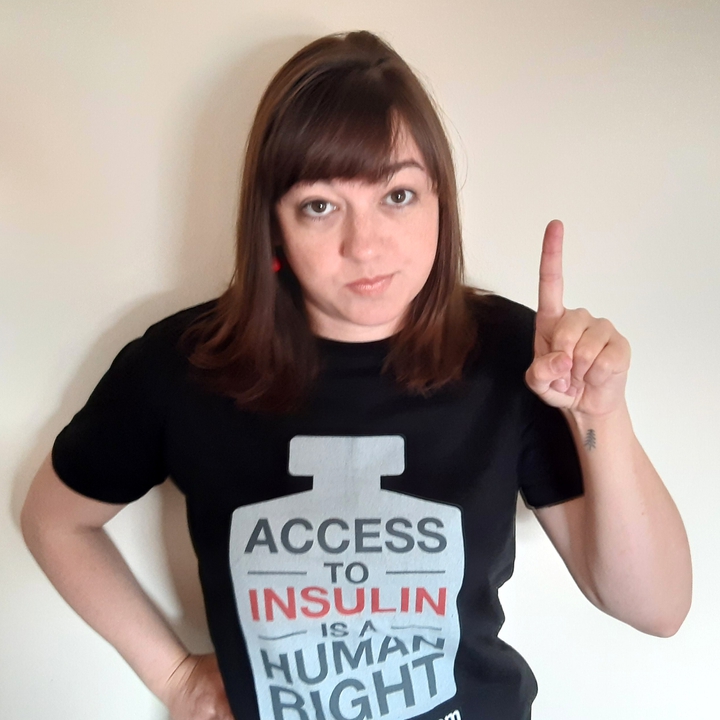 Liz looking seriously at the camera with one finger up and an Access to Insulin is a human right shirt