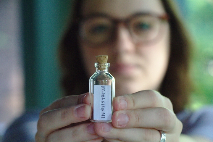 Liz holding a vial with a strip of paper saying "Living in the USA"