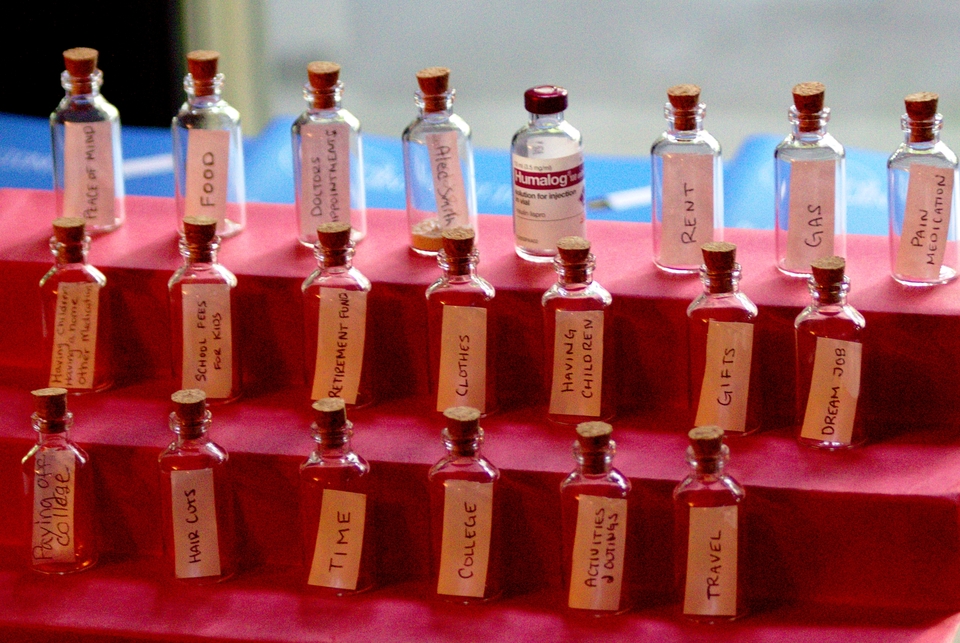 A set of dozens of vials with strips of paper in them saying what we've lost from high insulin prices on a red background