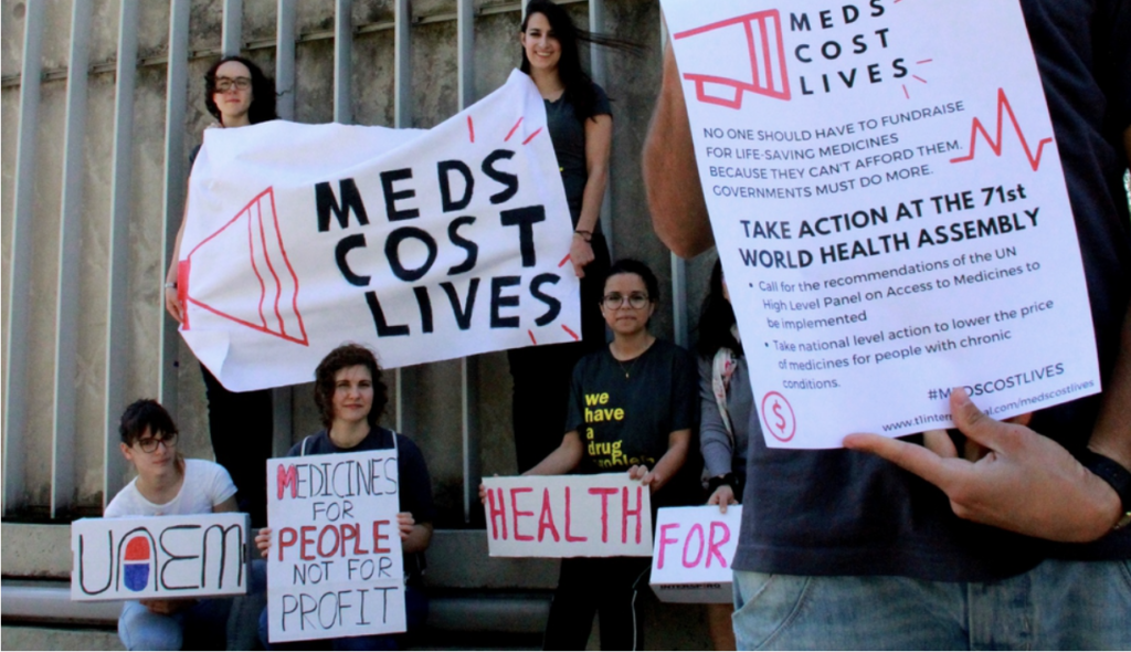 People holding white signs and banners saying Meds Cost Lives