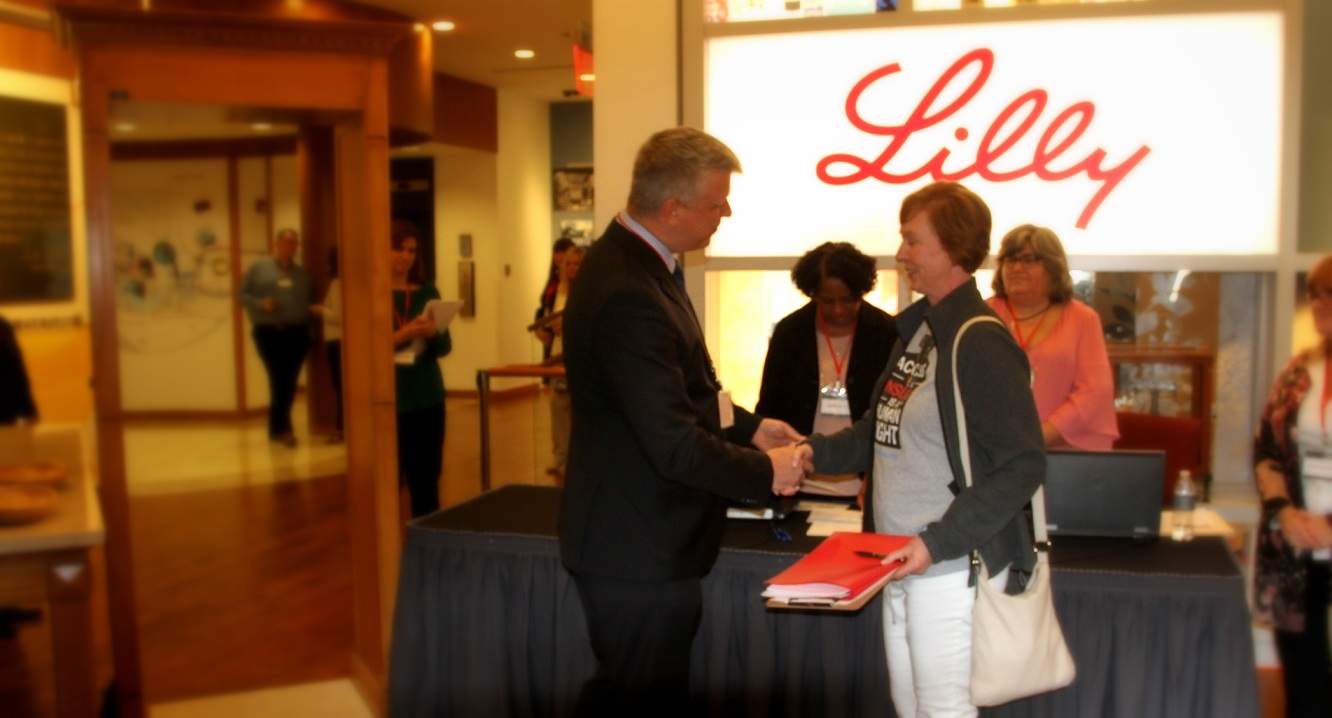 Nicole shaking the CEO's hand in front of neon Lilly sign