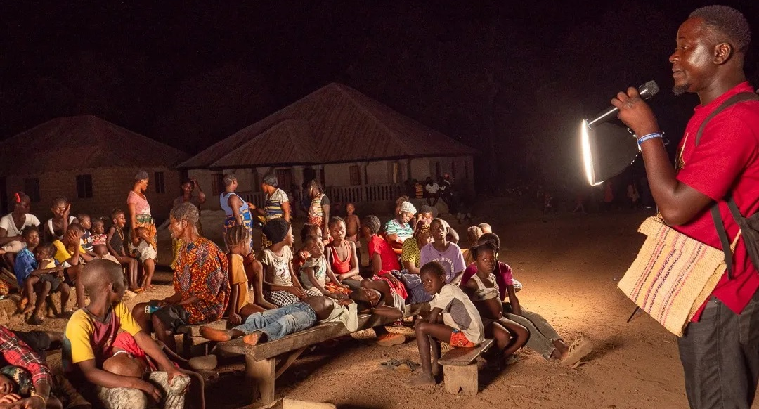 Speaking at a group of people at a film screening in Sierra Leone